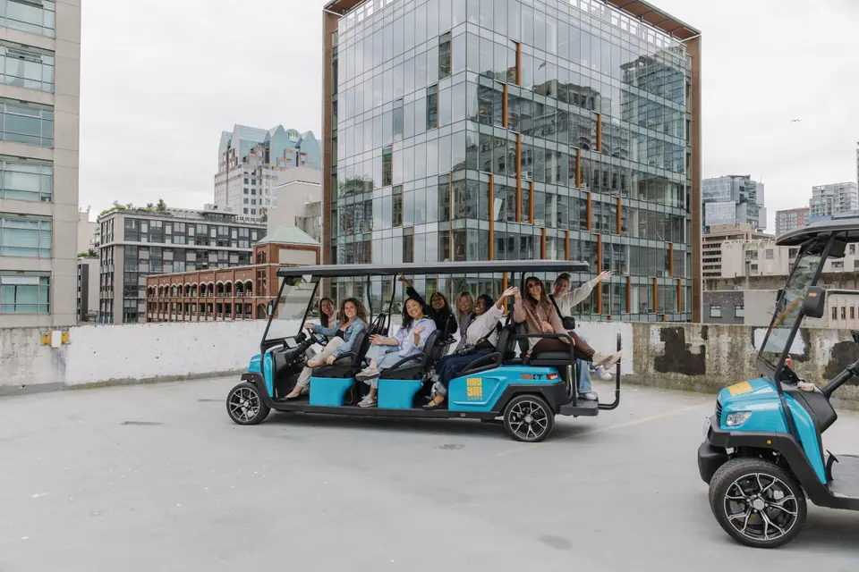 Friends waving from an eight-seat HeyYa cart on a downtown Vancouver rooftop, with a second cart in the foreground