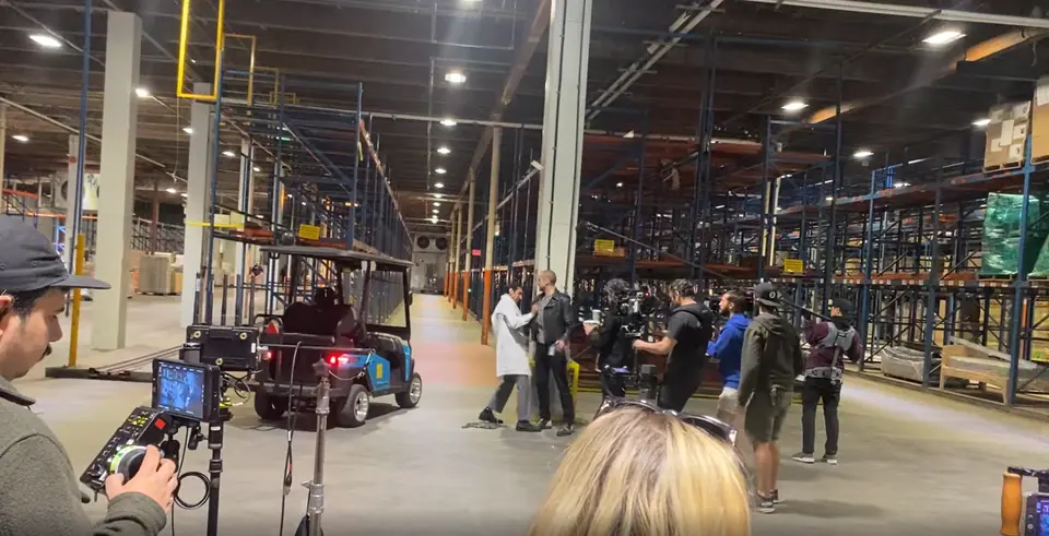 A film crew working on a warehouse set with a HeyYa cart parked between the shelving