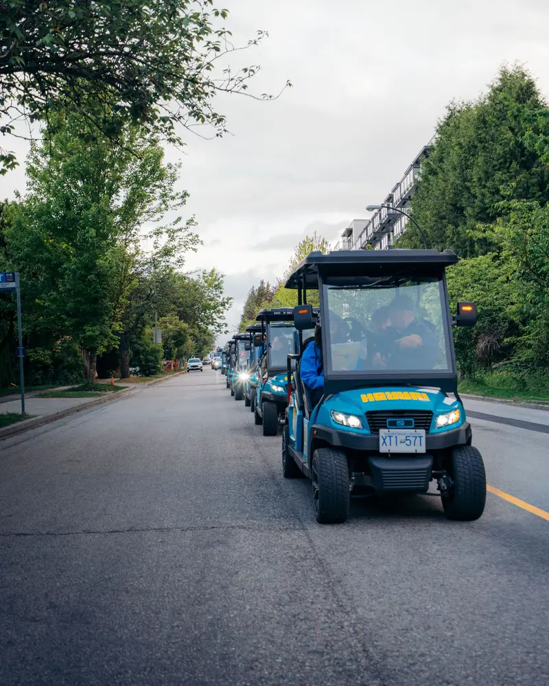 A HeyYa cart leading a convoy of carts along a tree-lined road