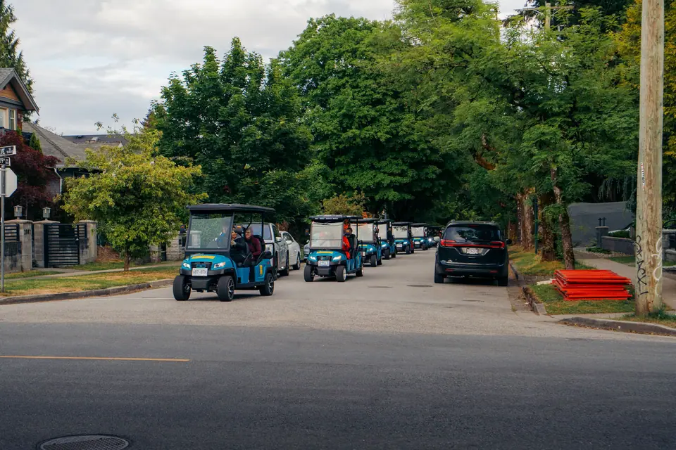A line of HeyYa carts travelling along a tree-lined Vancouver street during a community event