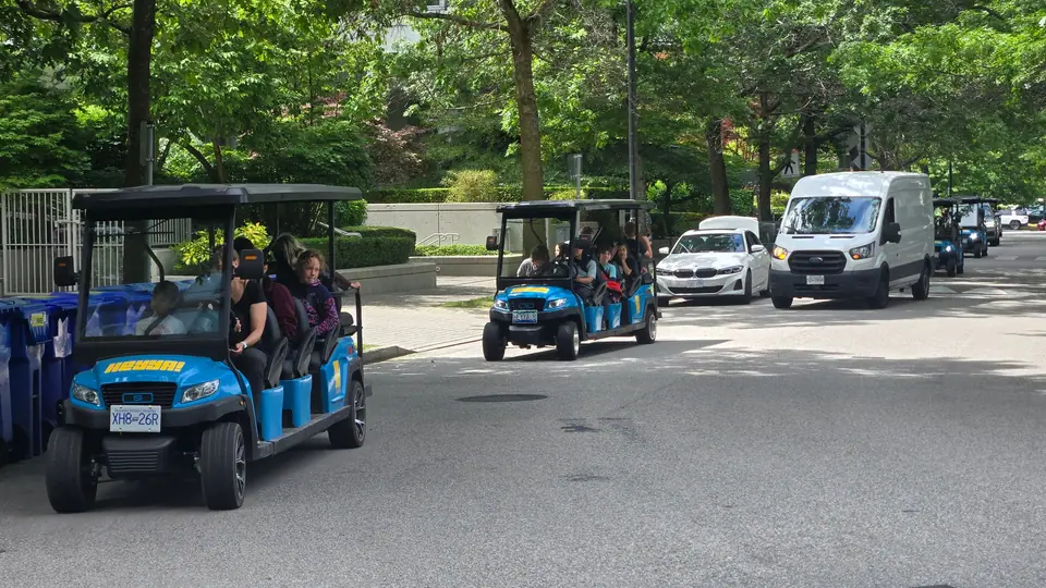Two eight-seat HeyYa carts carrying a group along a leafy downtown Vancouver street
