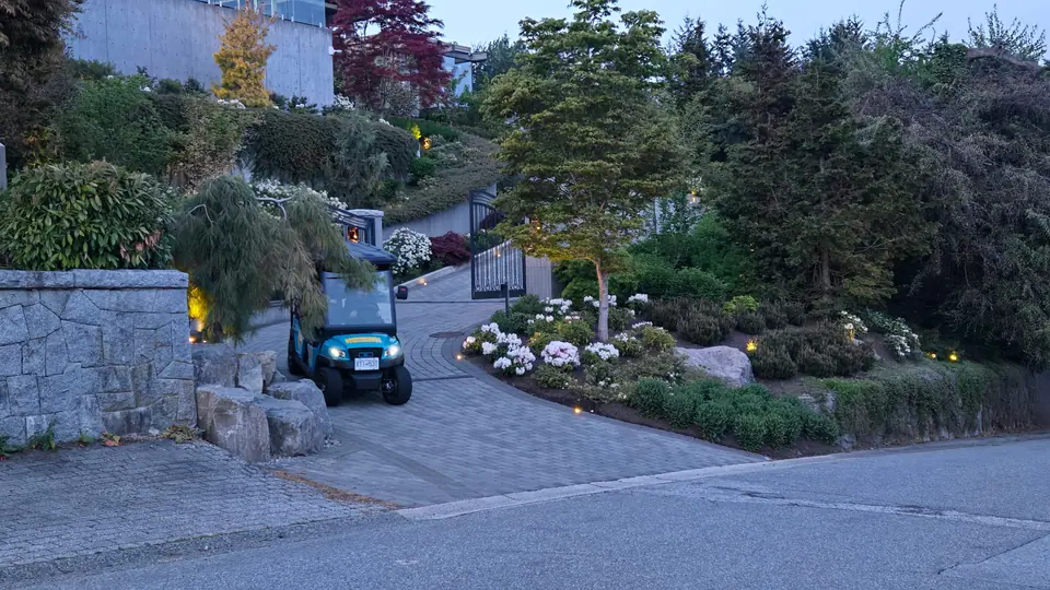 A HeyYa cart with headlights on rolling down a landscaped driveway at dusk
