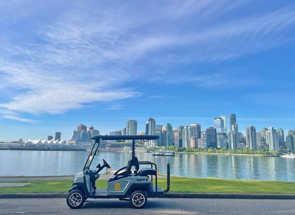 A HeyYa cart parked on a Stanley Park road with the downtown Vancouver skyline and Canada Place across the harbour