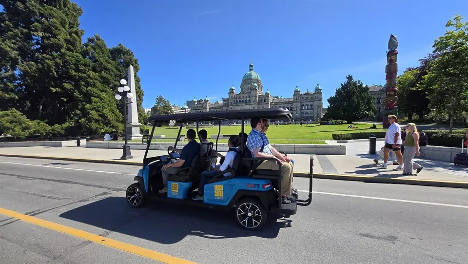 Passengers riding a HeyYa cart past the BC Parliament Buildings on a sunny day