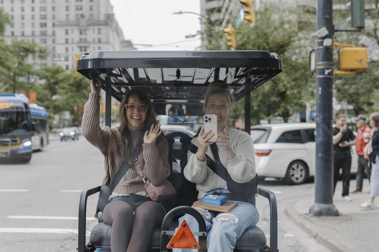 Two friends laughing and taking photos from the front seat of a HeyYa cart downtown