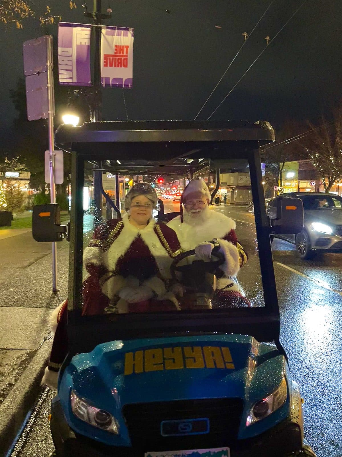 Two passengers dressed as Mr. and Mrs. Claus riding a HeyYa cart at night