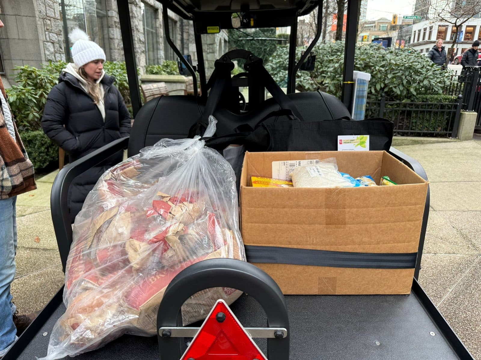 A bag of donated food and a box of supplies loaded on the back of a HeyYa cart